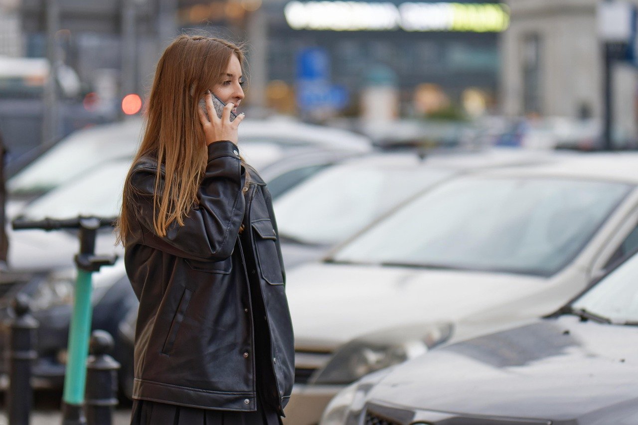 Mujer hablando por teléfono en la calle, junto a una hilera de autos estacionados
